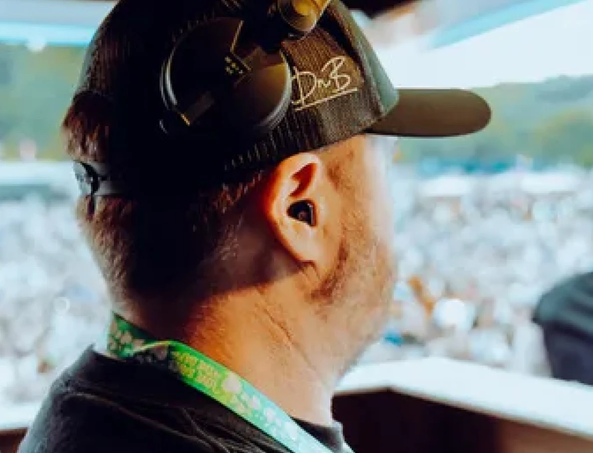 DJ wearing headphones overlooking a festival crowd, capturing the excitement of a live outdoor music event.