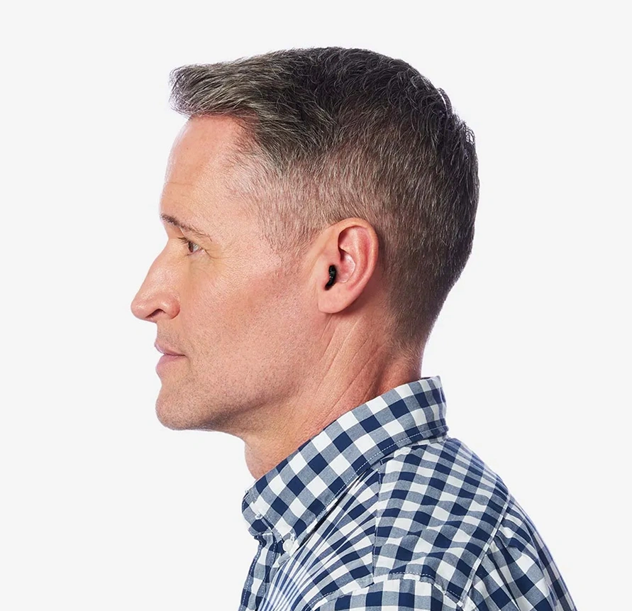 Profile of a man wearing a hearing aid, checkered shirt, white background.