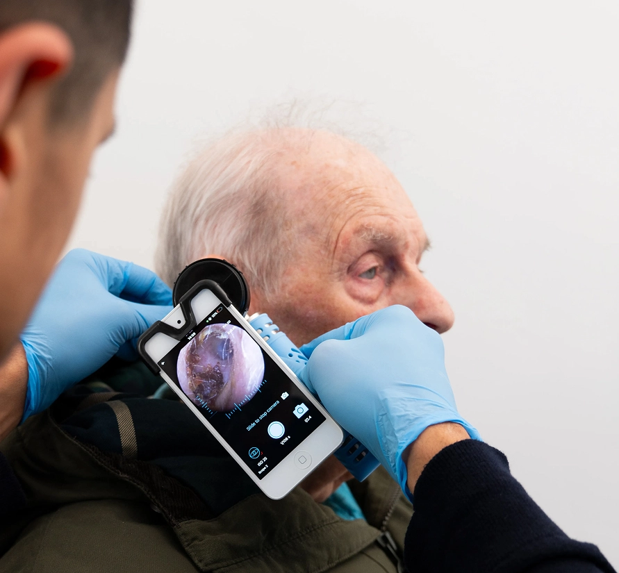 Doctor examines elderly man's ear with smartphone otoscope.