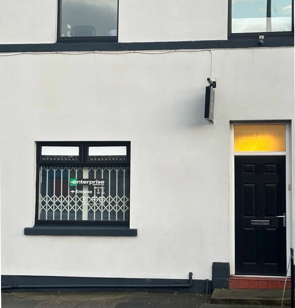 Exterior of a white building with a sign indicating Enterprise and entrance directions on a window.