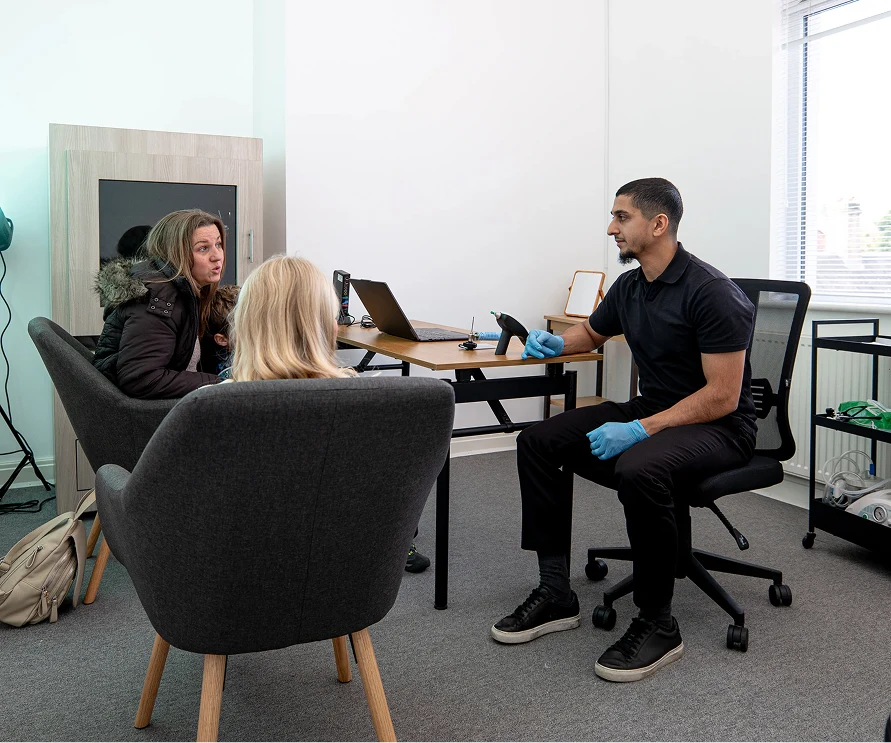Doctor consulting with two women in a medical office, wearing gloves and holding a medical device.