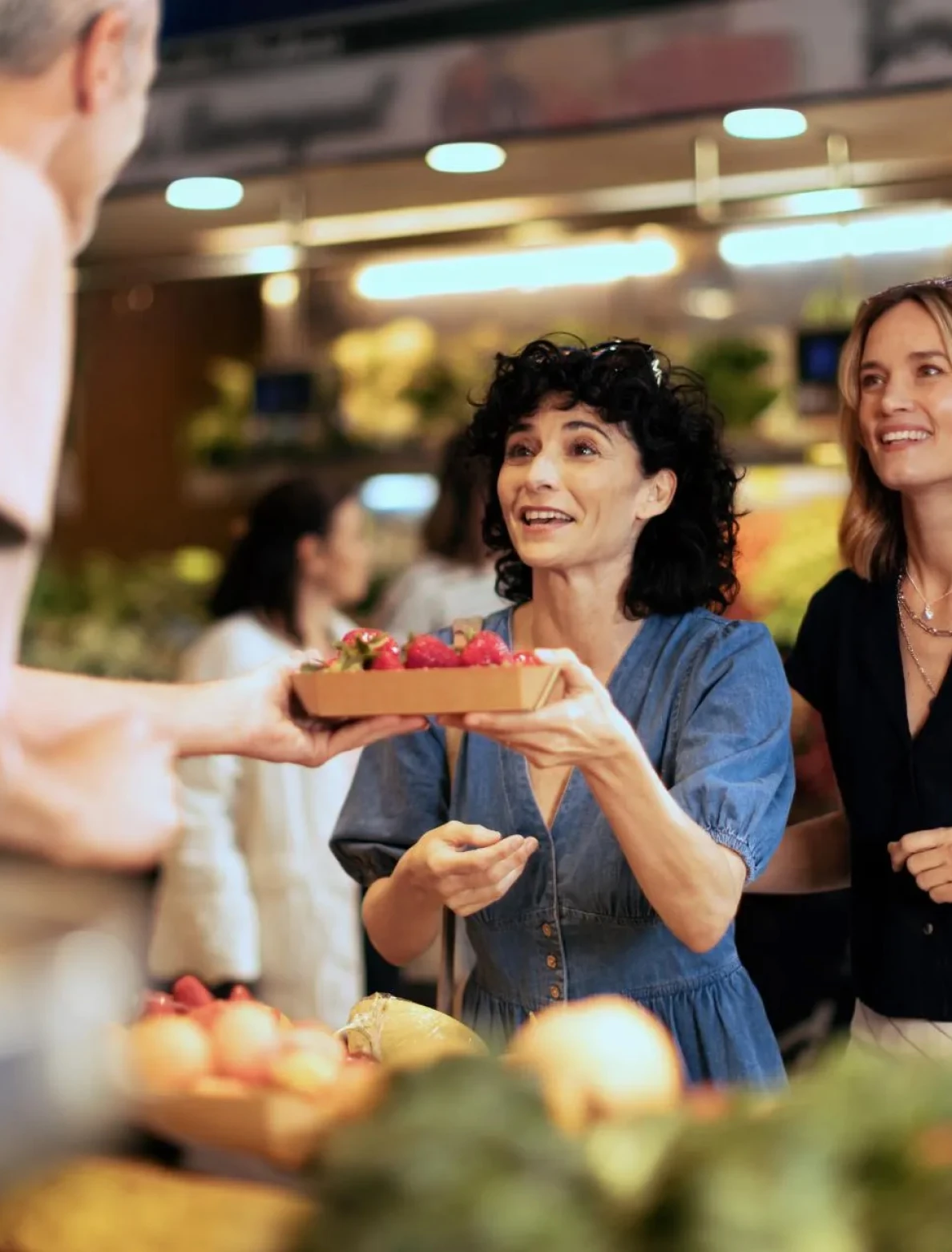 Two women smiling while buying fresh strawberries at a vibrant local market.