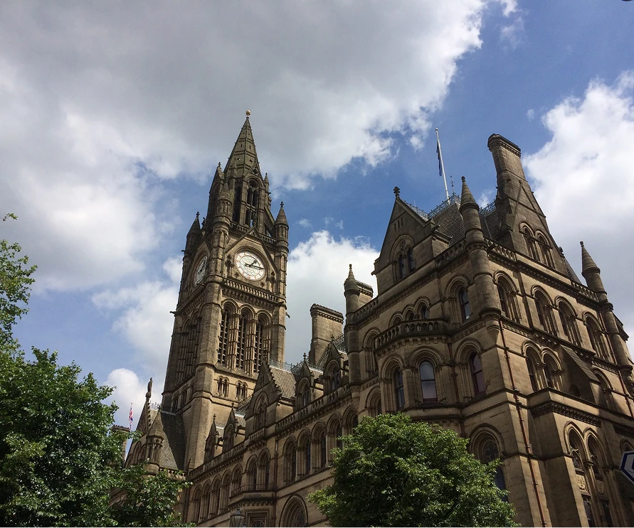 Historic clock tower and ornate architecture under a blue sky in Manchester, England.
