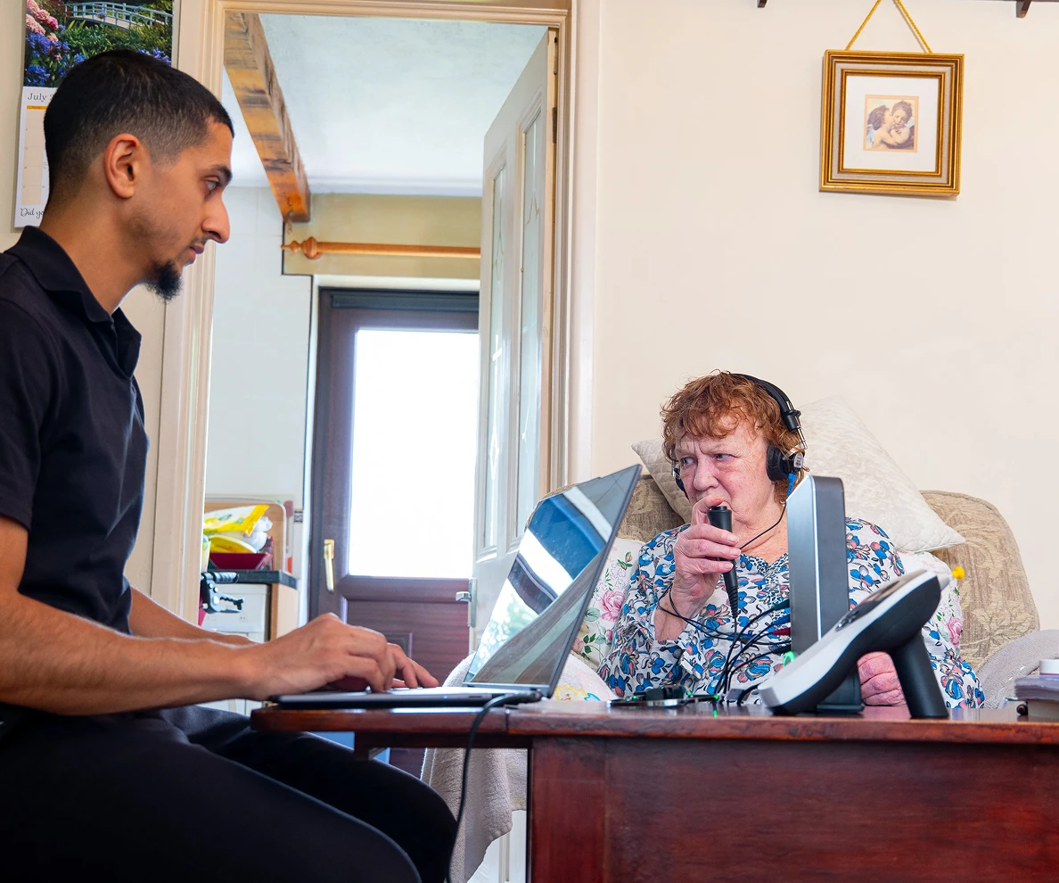 Healthcare professional assists elderly woman using respiratory equipment at home.