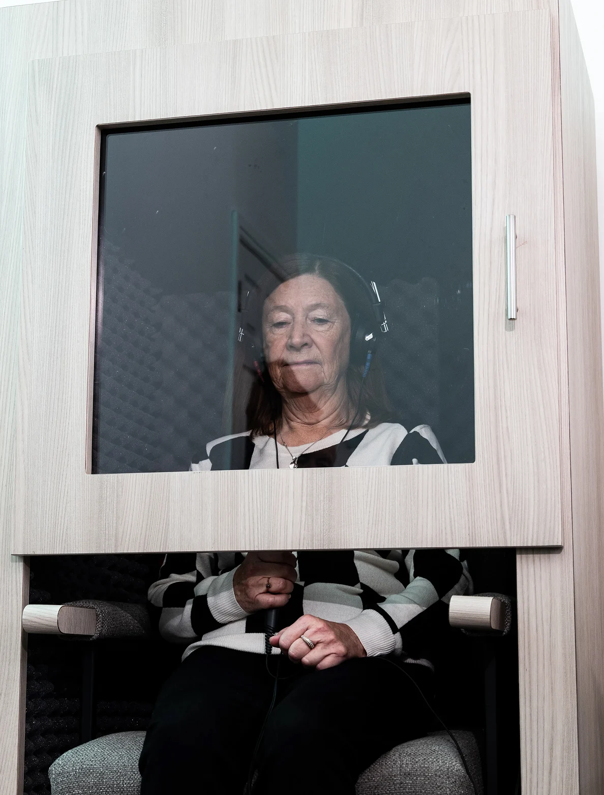 Woman undergoing hearing test in soundproof booth, wearing headphones and holding a sensor, testing for audiometry.