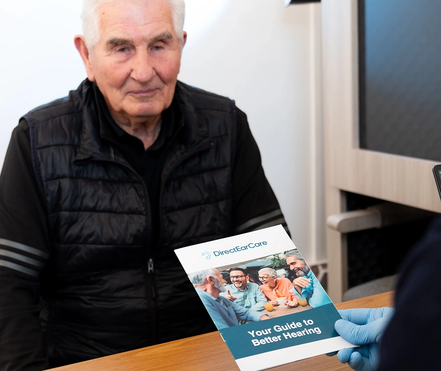 Elderly man receiving a brochure on hearing care titled Your Guide to Better Hearing from healthcare professional.