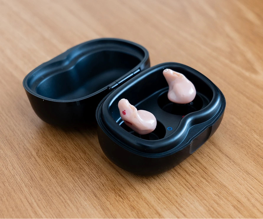 Wireless earbuds in a black charging case on a wooden table.