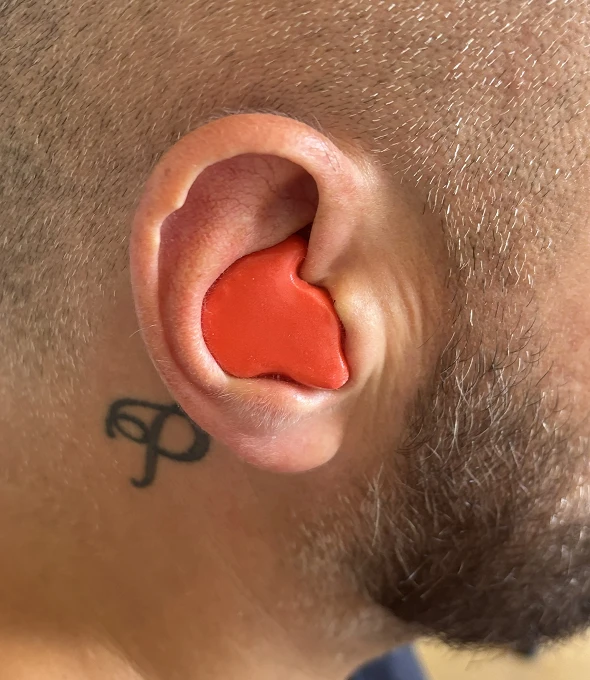Close-up of custom red earplug in a man's ear, next to a small neck tattoo.