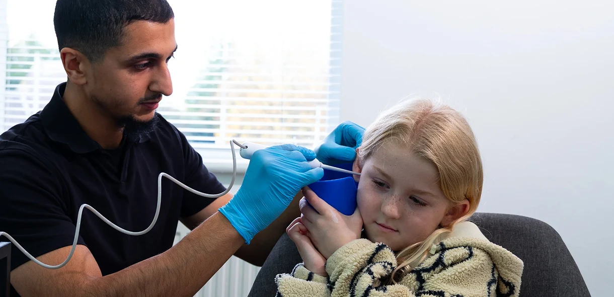 Child getting ear examination by a healthcare professional in a clinic setting.