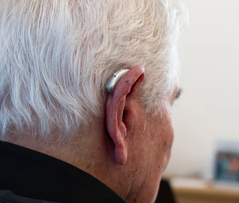 Elderly person wearing a modern hearing aid behind the ear, close-up view.