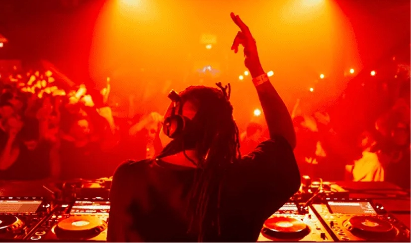 DJ performing in a vibrant club with a cheering crowd, illuminated by red lights.
