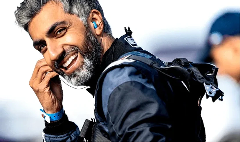 Smiling man with earbuds, wearing a parachute suit, prepares for skydiving.