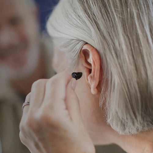 Person inserting modern black hearing aid into their ear for enhanced hearing experience.