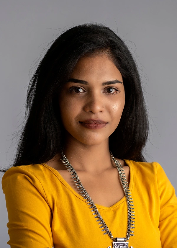 Portrait of a woman in a yellow top and necklace against a gray background, showcasing confidence and style.