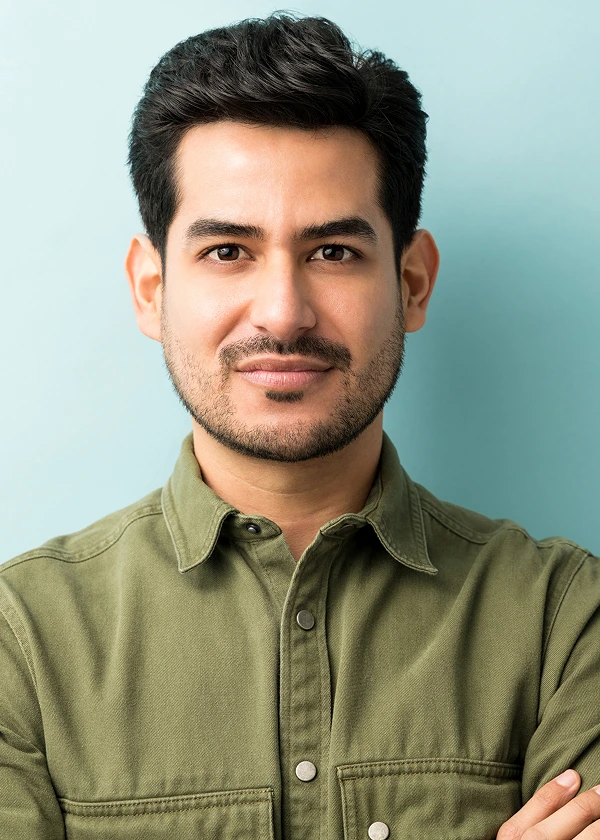 Man in a green shirt smiling confidently with a light blue background.