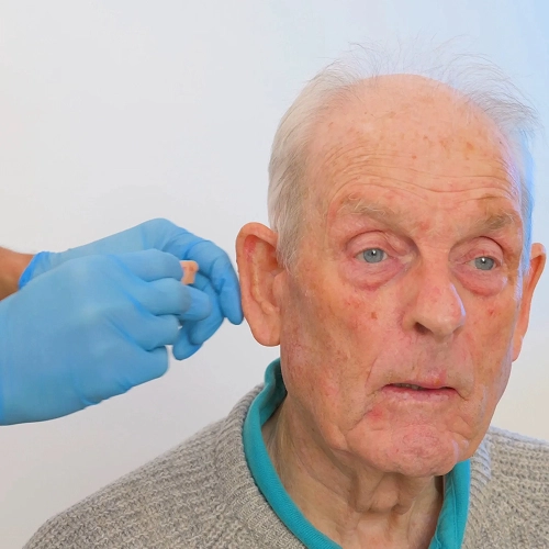 Elderly man receiving a hearing test with device, assisted by gloved professional.