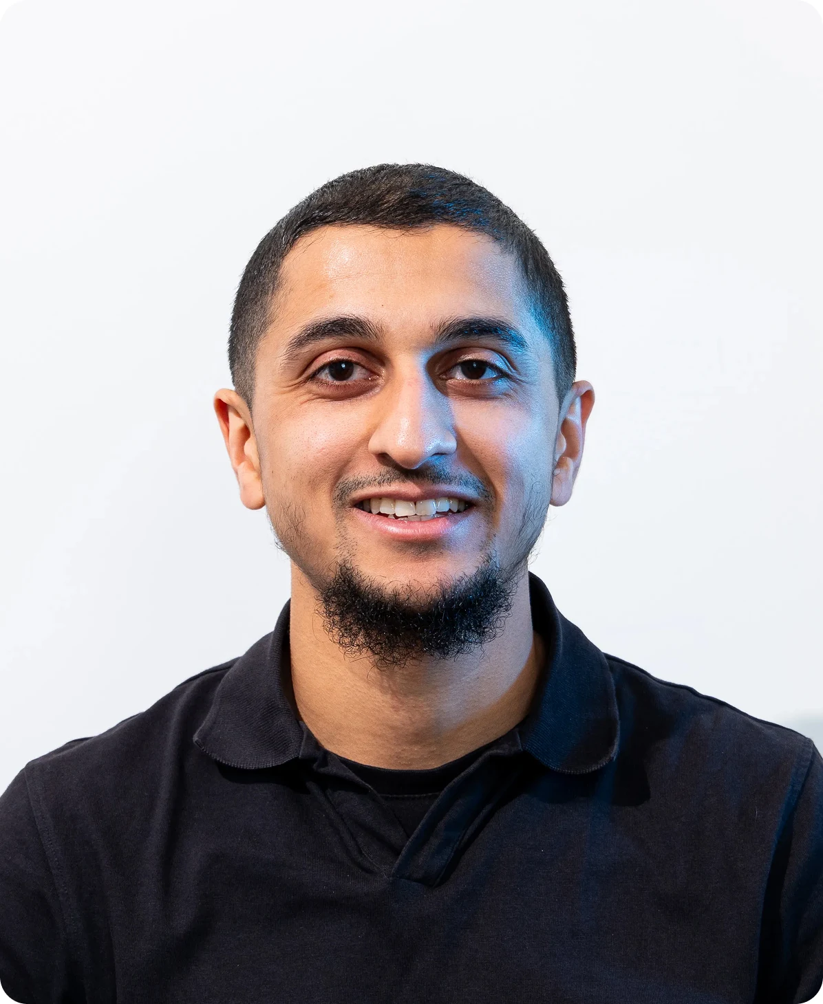 Smiling man in black shirt against plain background, looking forward.