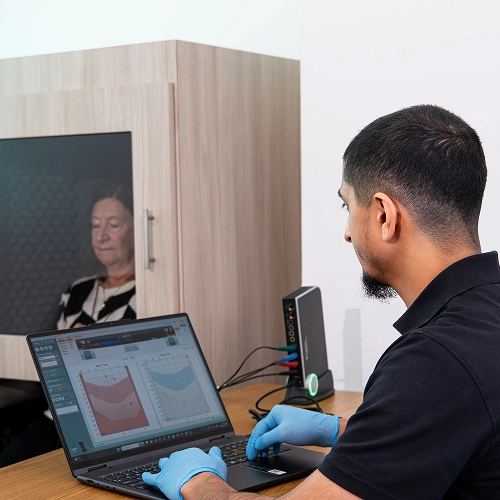 Technician conducts an audiology test on an elderly woman using specialized equipment and a laptop.