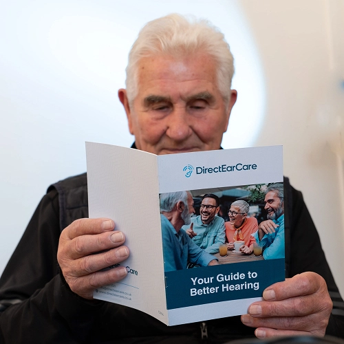 Elderly man reading DirectEarCare guide on improving hearing health and solutions.