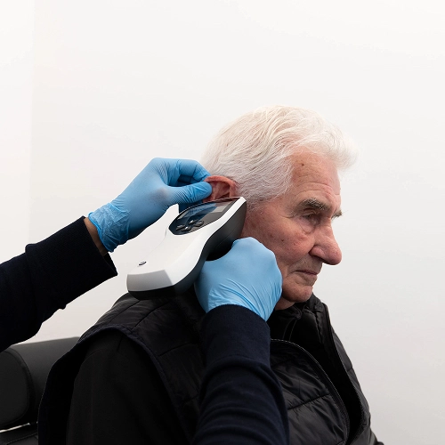 Hearing test in progress: Professional examining an elderly man's ear with modern audiology equipment.