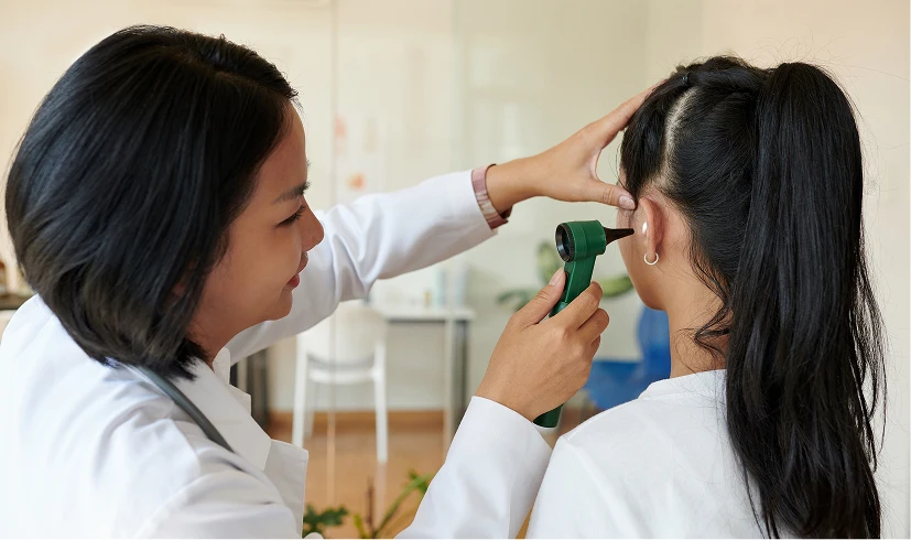 Doctor examining a patient's ear with an otoscope in a medical office setting.