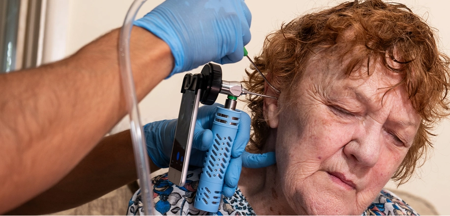 Elderly woman receiving ear care with otoscope, gloved hands, close-up.