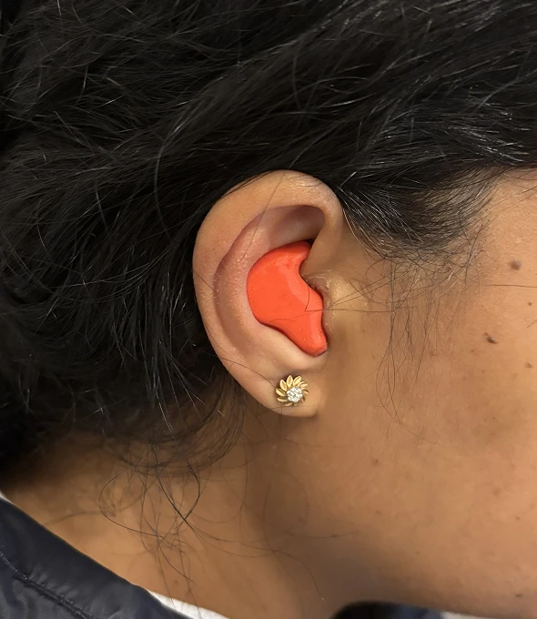 Woman with red earplug wearing floral earring, side profile view.