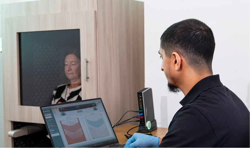 Audiologist conducting a hearing test with patient inside soundproof booth.
