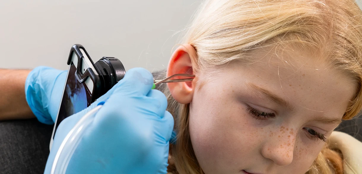 Child's ear examined with a smartphone device by gloved professional, highlighting ear care and health technology.