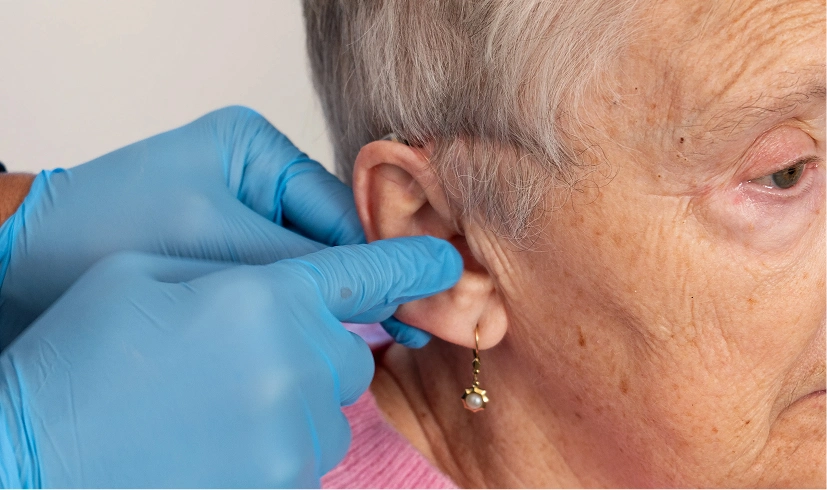 Close-up of a healthcare professional checking the ear of an elderly woman wearing blue gloves and a pearl earring.