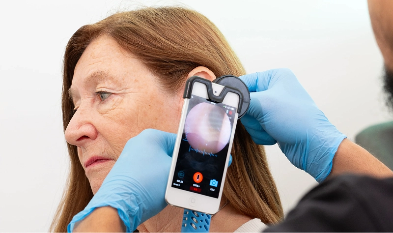 Healthcare professional using smartphone otoscope to check a patient's ear.