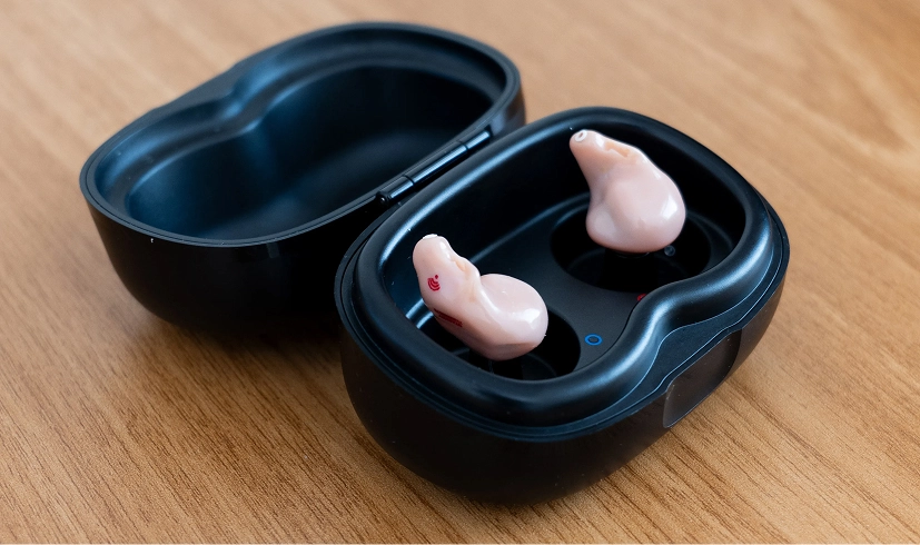 Earbuds in a black charging case on wooden table, showcasing sleek design and portability.