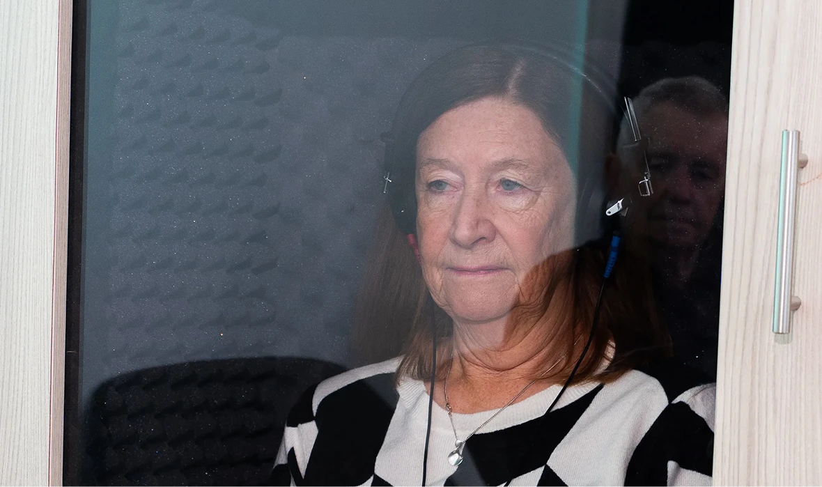 Woman recording in soundproof booth with headphones, focused expression, studio setting.