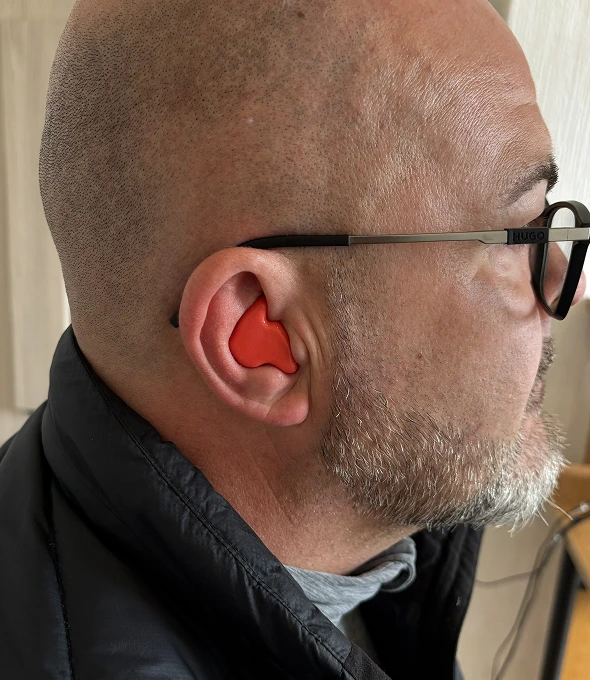 Man wearing red earplug and glasses, side view, bald head with beard.
