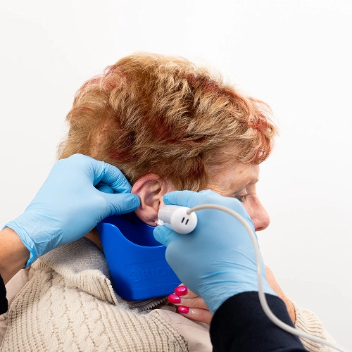 Elderly woman receiving ear exam with blue device and gloved hands in medical setting.