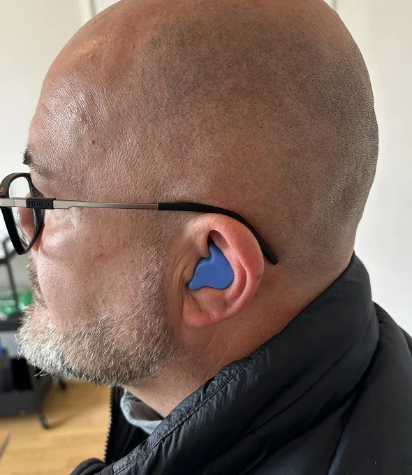 Man wearing blue ear protection and glasses indoors.