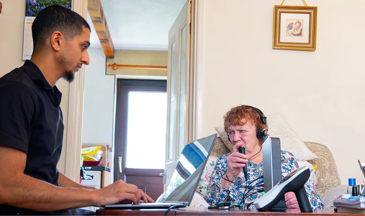 Home healthcare worker assisting elderly woman with telehealth equipment.