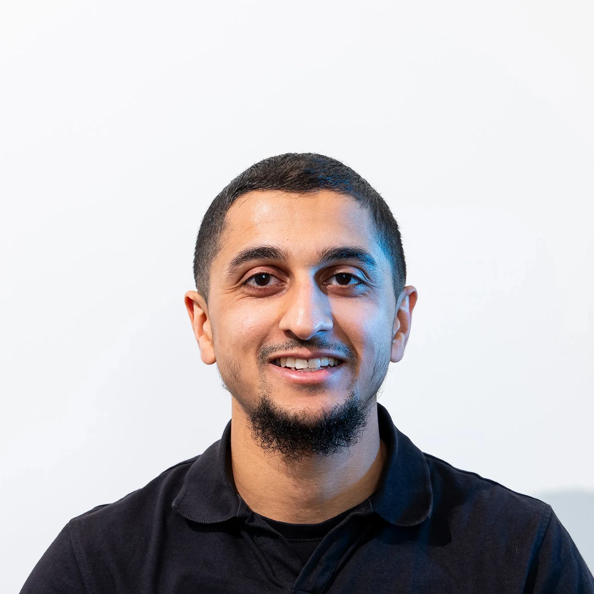 Smiling man in a black shirt standing in front of a plain white background.
