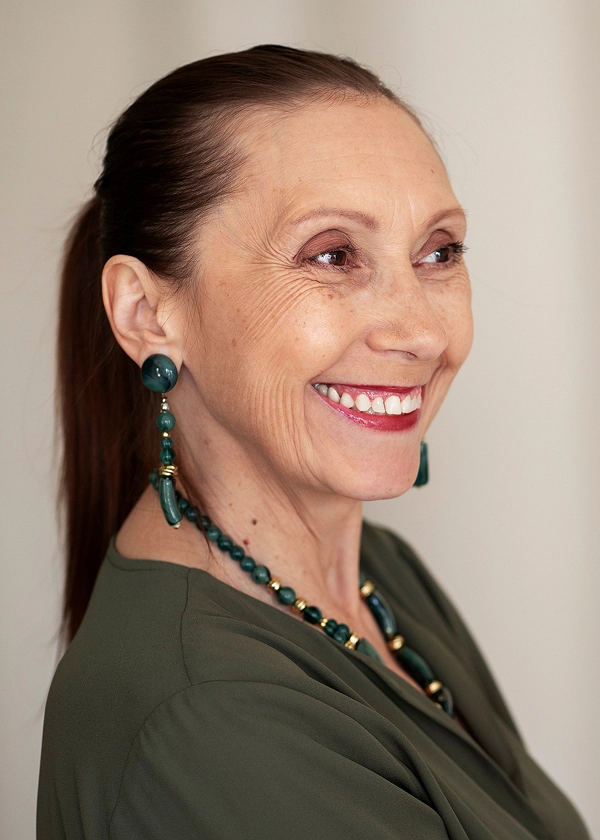 I'm not sure who they are, but here's an alt text: Smiling woman with dark hair, wearing green outfit and jewelry.