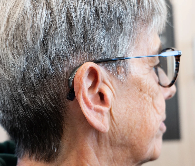 Senior woman wearing hearing aid and glasses, side profile view.