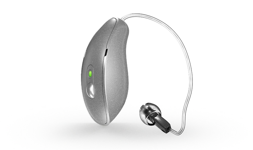 Silver hearing aid with green indicator, featuring a wire and earbud, isolated on a white background.