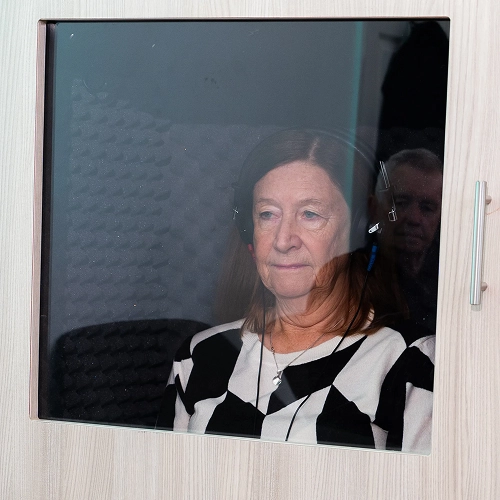 Woman wearing headphones inside a recording booth, focusing on audio.