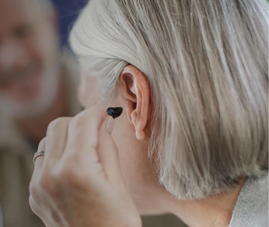 Person inserting a modern hearing aid into the ear, improving hearing ability with advanced technology.