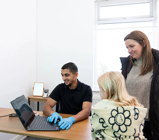 Doctor consults two patients in office, using laptop for digital medical advice.