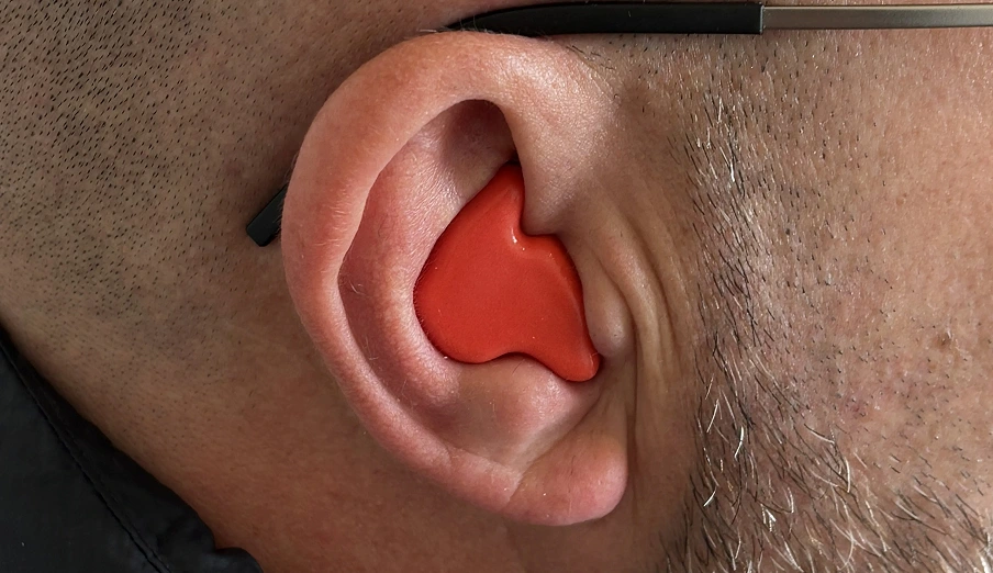 Close-up of a person wearing a red earplug for noise reduction or hearing protection.