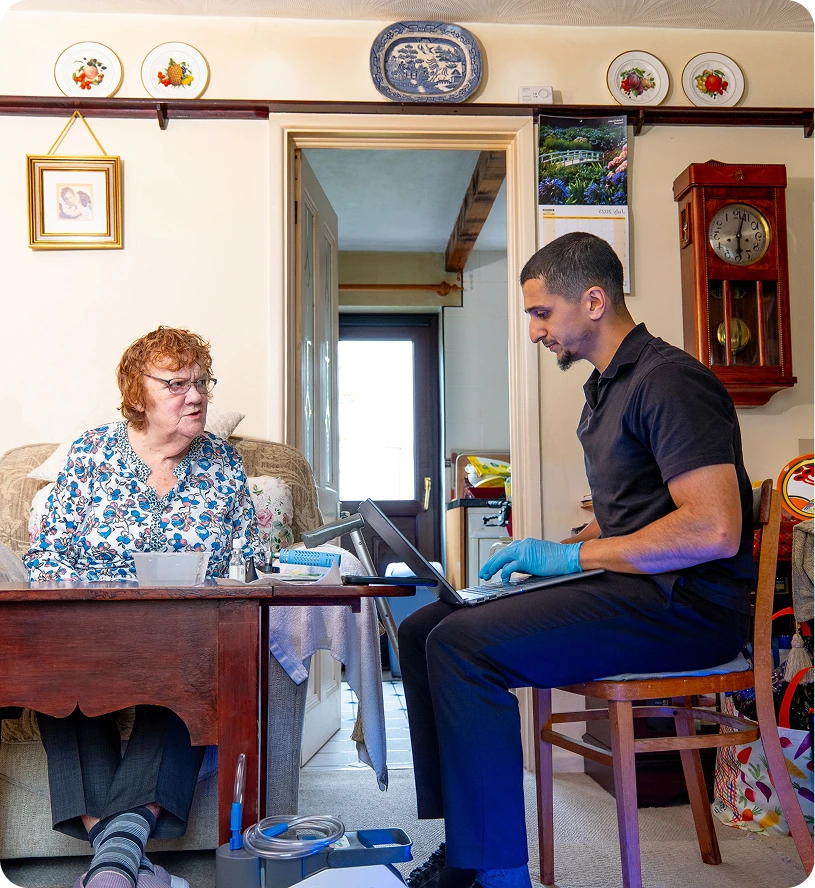 Healthcare worker assists elderly woman in home visit, discussing medical needs. Cozy living room, caring interaction.