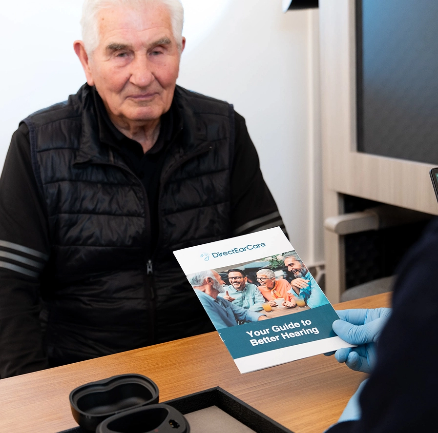 Elderly man receiving a brochure on better hearing care from a professional at DirectEarCare clinic.