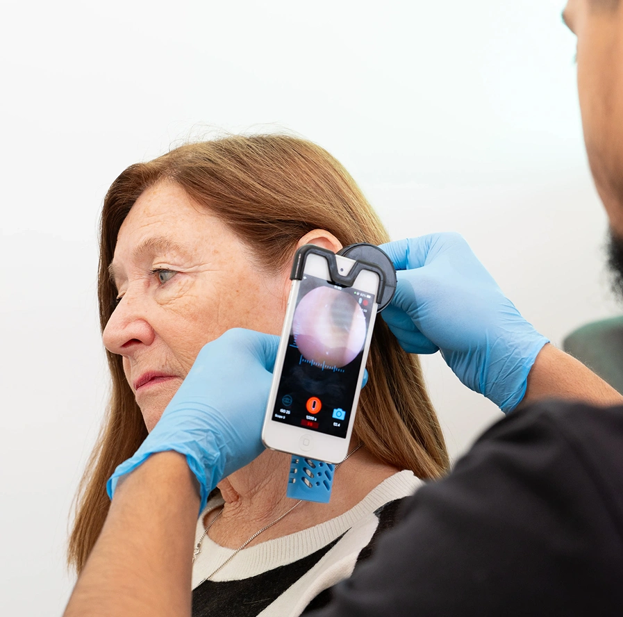 Doctor using a smartphone otoscope to examine a patient's ear canal.