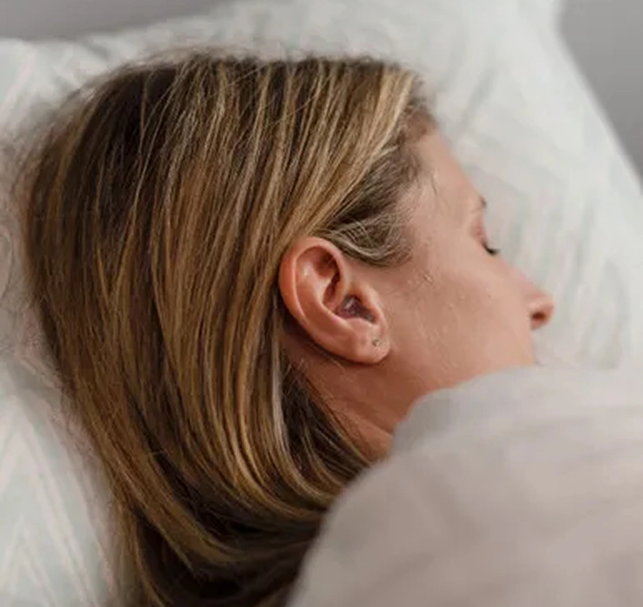 Sleeping woman with blonde hair resting peacefully on a white pillow.